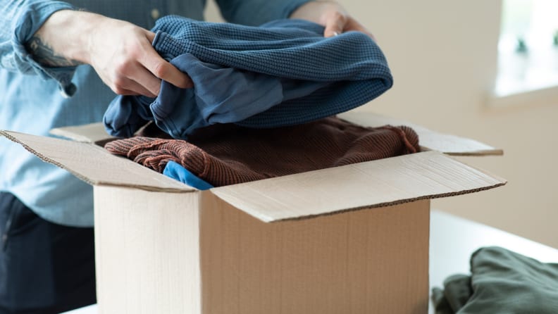 Person placing folded clothing items in box to donate.