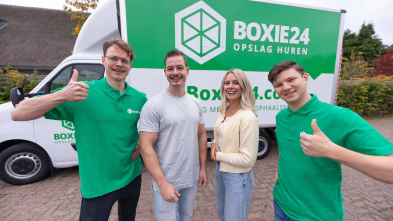 Four people give thumbs up in front of a white and green truck