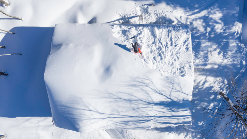 A person clears snow from a roof with a shovel.