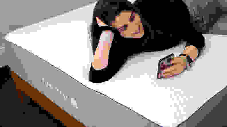 a woman lies on her phone on the Nectar mattress