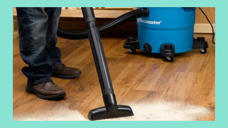 Someone is using a VacMaster to clean up spilled sand on a hardwood floor.