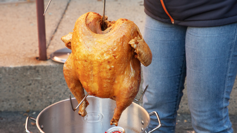 A person taking a golden brown deep fried turkey out of the pot.