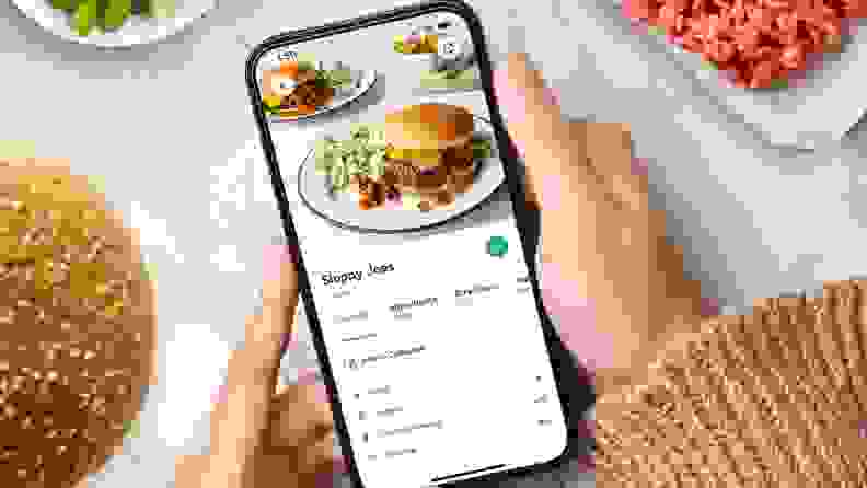 A hand holding a smartphone displaying the Yummly app.