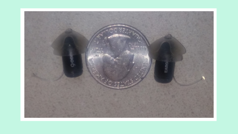 Set of black Eargo 6 hearing aids next to quarter for size scale.