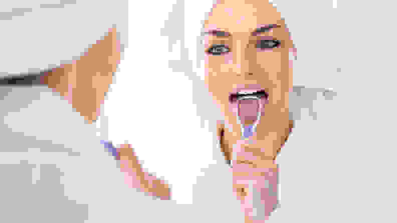 A photo of a woman using a tongue scraper.