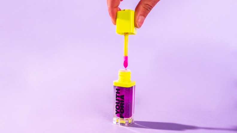 The purple and yellow Dewy Gloss tube sits against a lavender background.