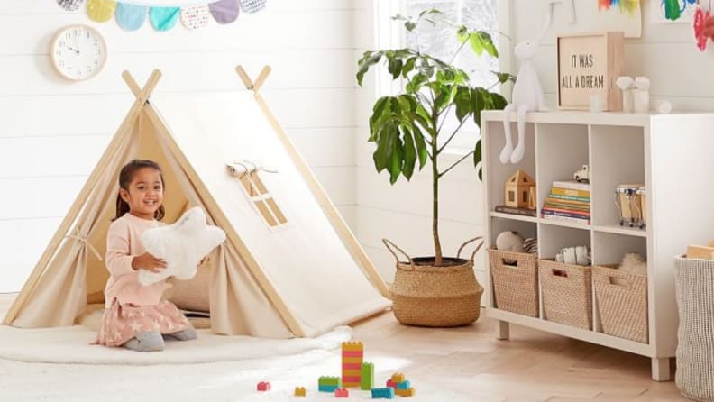 Cube storage organizer in child's room as child plays with stuffed pillow.
