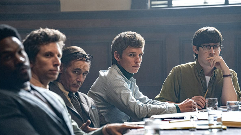 A still from The Trial of the Chicago 7 that features the cast seated at a table looking to camera.