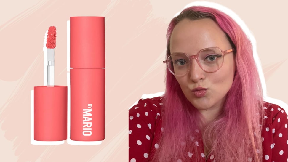 On the left: A coral-colored doe-foot applicator and lipstick tube. On the right: A person with pink hair wearing a red top and glasses purses their lips, which has a pink color on it.