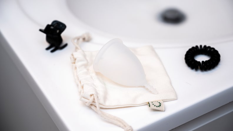 AllMatters (oficialiai OrganiCup) menstruacinė taurelė balto marmuro fone.