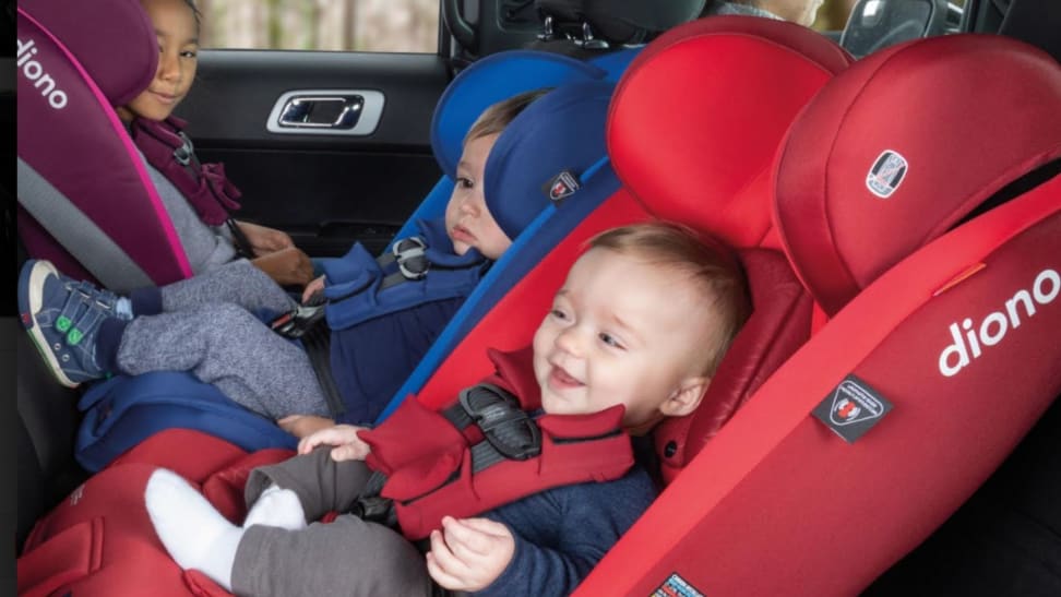 Three children sit in the same Diono car seat. All are different ages and the car seat is in purple, blue, and red.