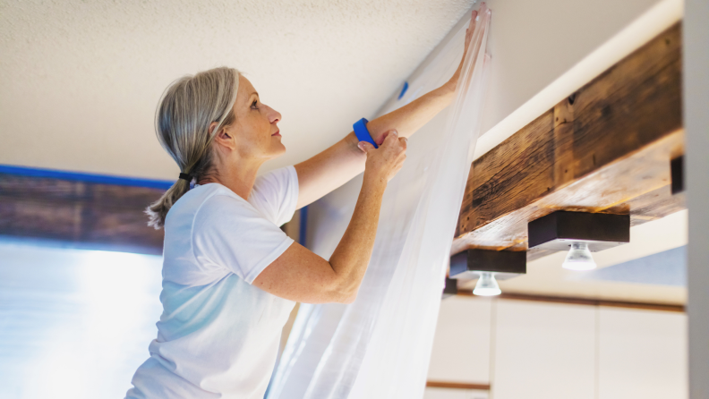 Woman hanging up plastic with painters tape before painting.