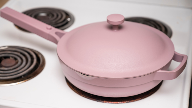 A pink Always pan sits on a stove.