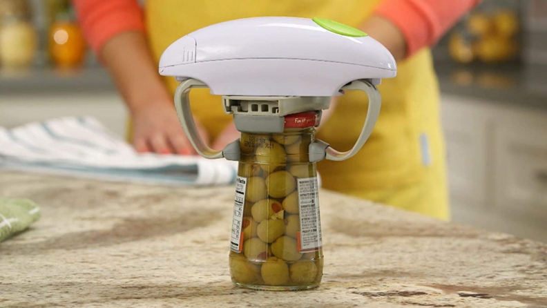 A Robo Twist jar opener placed above a jar of olives.