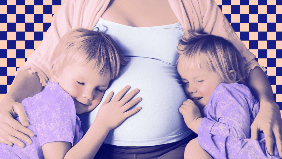 Two small child rest against pregnant mother's baby bump with eyes clothes, while mother has their arm around them.