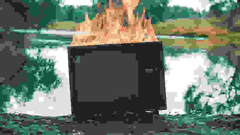 Retro vintage TV is on fire next to a pond. Concept of post apocalypse, surrealism and the fire hazard of old worn out equipment
