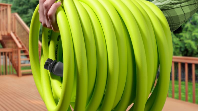 A man holds a coiled up green Flexilla garden hose