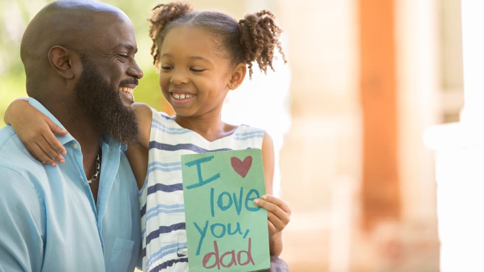 Girl sitting on her dad's lap holding a card that says "I love you dad"