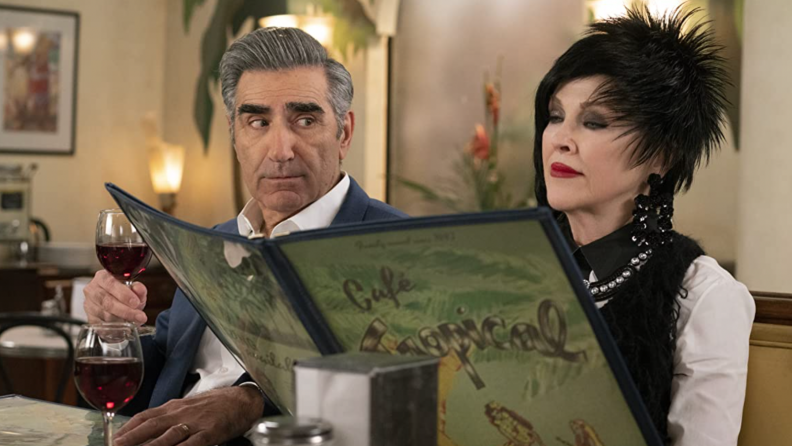 A still from Schitt's Creek that features Moira and Johnny rose sitting in a diner reading a menu.