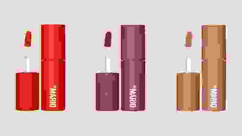 Red-, plum-, and beige-colored lipstick tubes with doe-foot applicators stand against a pink background.