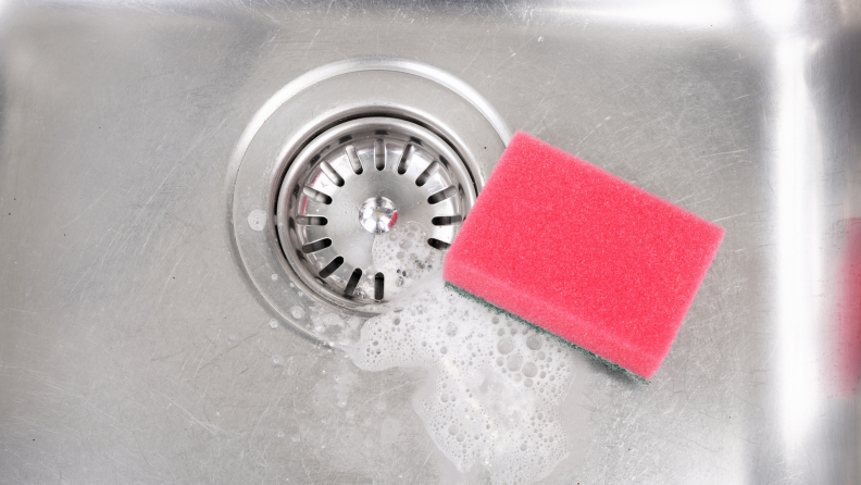 A pink sponge sits in a stainless steel sink.