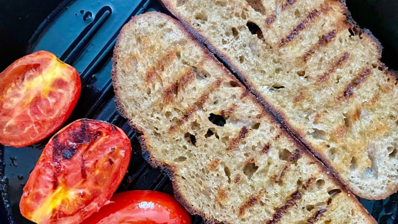 Tomatoes and slices of sourdough bread grill on a cast-iron grill pan.