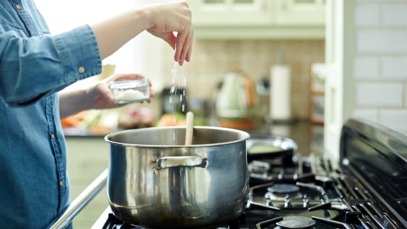 A hand sprinkling salt into a pot on the stove.