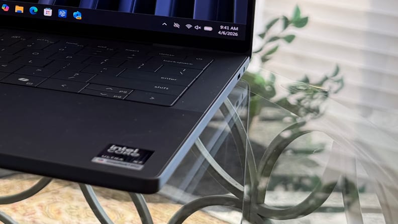 Close-up photo of side of Dell XPS 14 2026 laptop showing ports, atop a glass table with green plants in the background.