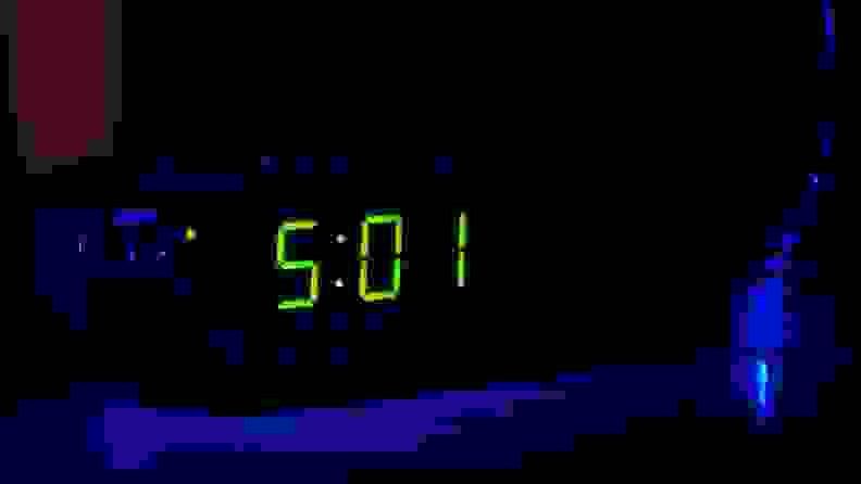 a digital alarm clock with a green display on a side table