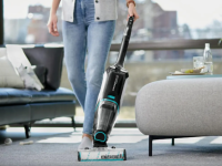 Person using vacuum to clean carpeted floors in living room at home next to couch.