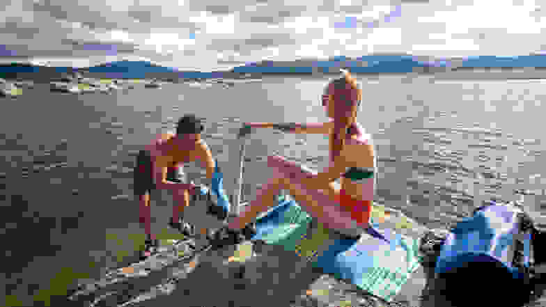 Two people sitting on a towel by a lake.