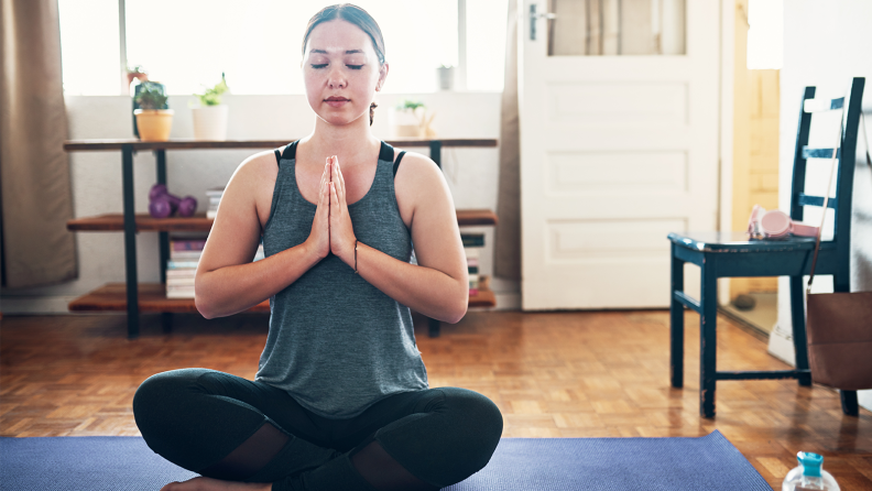 A woman in exercise clothes sits with her legs crossed and eyes closed