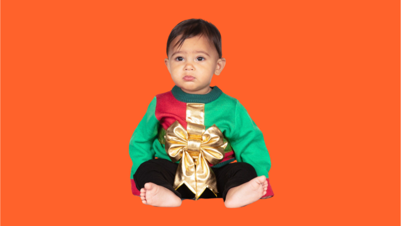 A baby wears an ugly Christmas sweater that looks like a present.