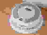 A round, white smoke detector sits on a wood background