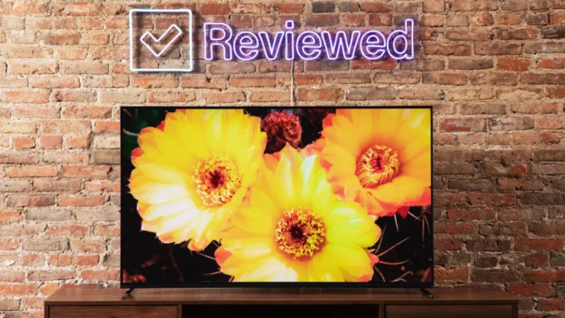 The Sony A80K on a TV stand with a brick background featuring yellow flowers on the TV.