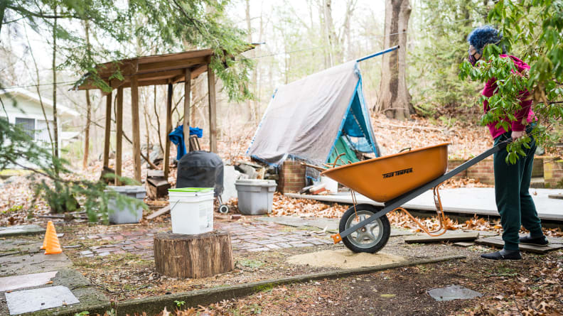 A person wearing a mask pushes a wheelbarrow through an obstacle course in the woods.