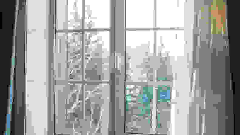 A view of an outdoor winter landscape through a window surrounded by flowing curtains.