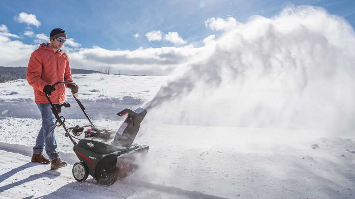 A person in winter wear demonstrates a Briggs and Stratton snow blower.