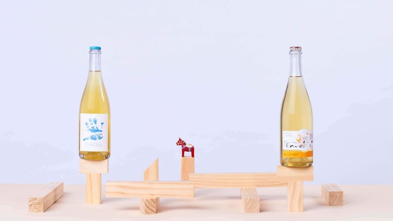 Two bottles of white wine perched on an elevated wooden platform against a white background.