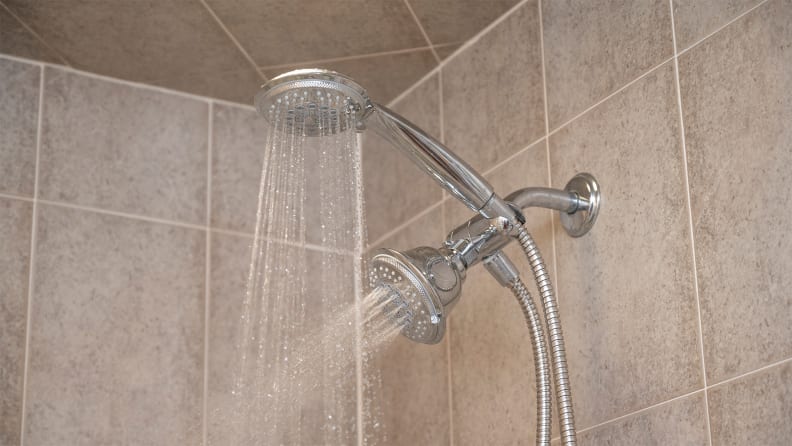 Handheld and permanent showerheads streams water in a beige-tiled shower stall.
