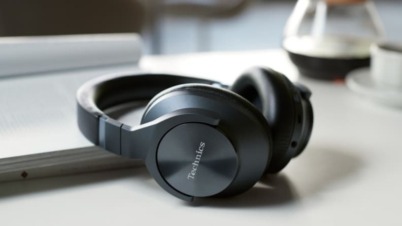 A pair of shiny, charcoal-colored over-ear headphones sit next to a computer on a modern desk.