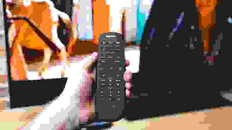 A hand holds a Logitech universal remote.