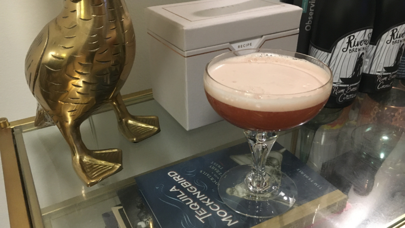 A bourbon cocktail in a coupe glass sits on a glass bar cart.