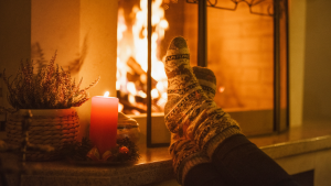 Fireplace and candle burning with someone's feet in socks kicked up against the fireplace