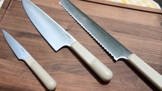 在我们店旁边的胡桃木砧板上，陈列着一套刀具。从左边开始，有一把削皮刀、一把厨师刀和一把锯齿切片刀。