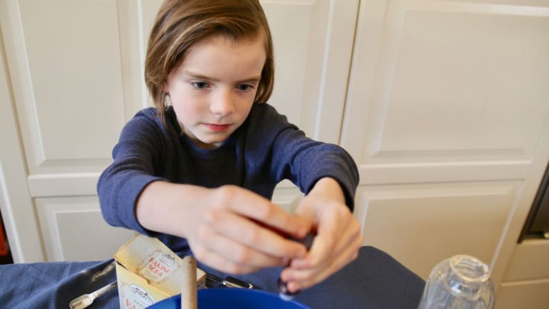 Young boy adding blue food coloring in blue bowl to slime.