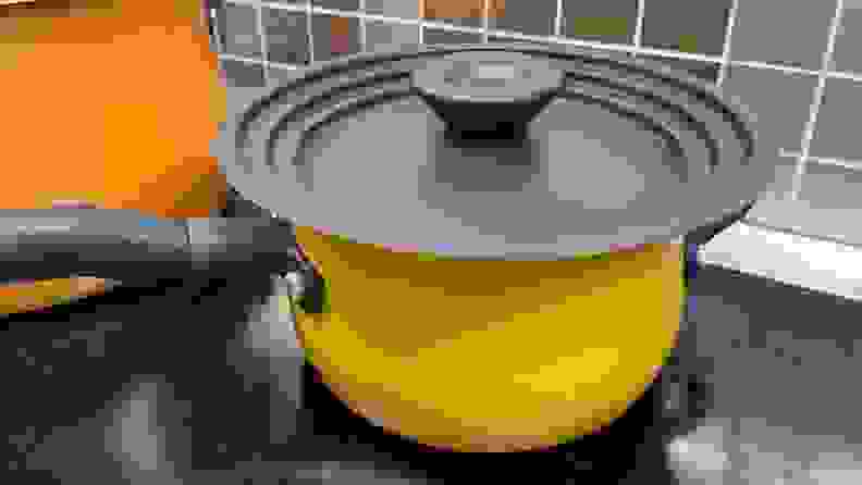 Small yellow pot with black lid sits on top of cooktop.