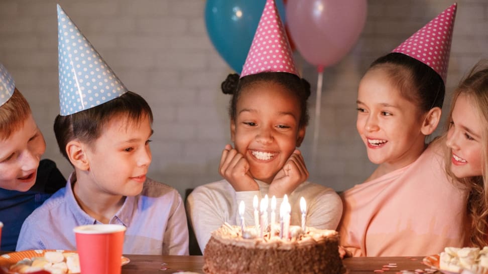 A happy Black girl smiles as her friends crowd around. She's ready to blow out birthday candles.