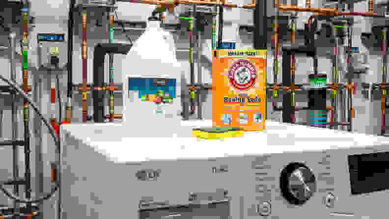 A jug of vinegar, a box of baking soda, and a sponge atop a washing machine