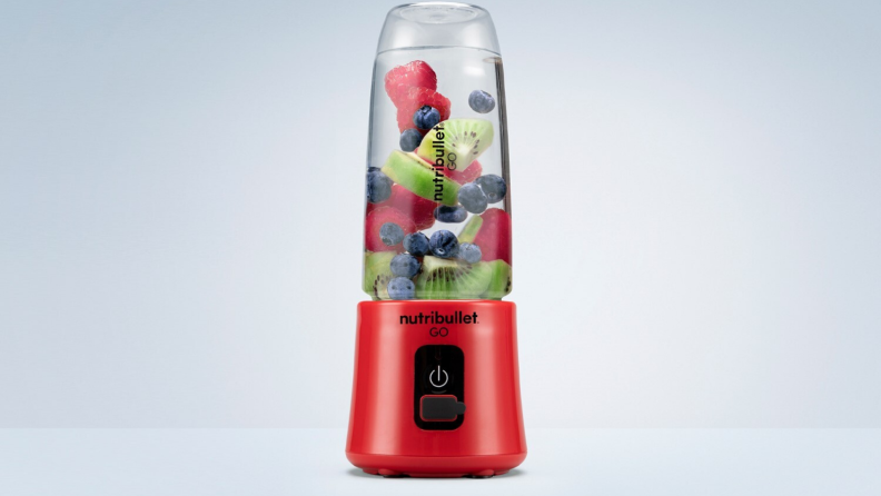A red NutriBullet Go blender contains kiwi, blueberries, and raspberries.